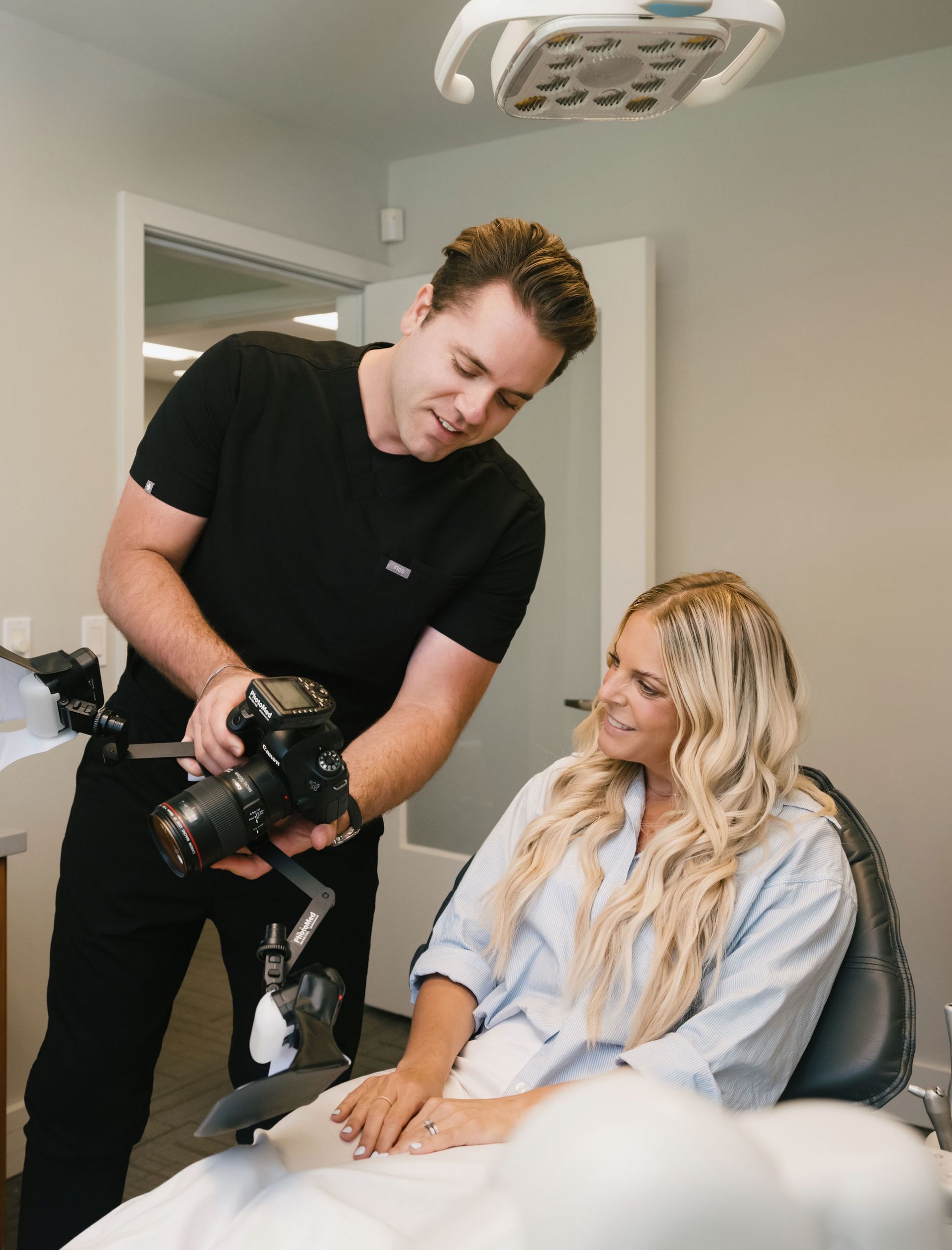 A male dental professional showing a camera photo to a smiling female patient seated in a dental chair.